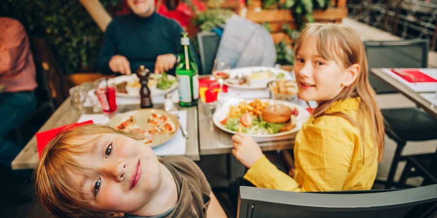 Happy family eating hamburger with french fries and pizza in outdoor restaurant